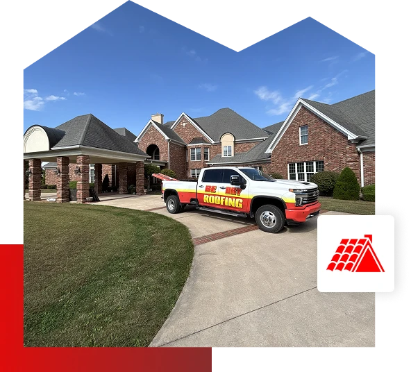 A Be Dry Roofing truck, representing professional roofing services, is parked in the driveway of a large brick house with multiple rooflines in Quincy, IL. The sky is clear and blue, with a red roofing icon in the lower right corner.