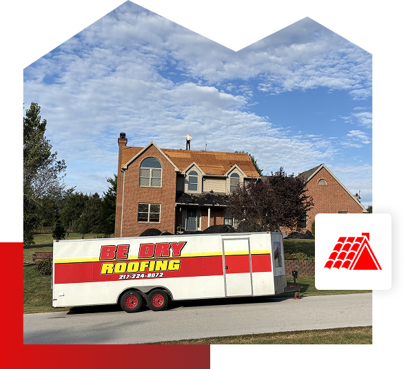 A large brick house in Quincy IL has roofers from Be Dry Roofing working on the roof. A trailer labeled BE DRY ROOFING is parked out front, showcasing their roofing services under a partly cloudy sky.