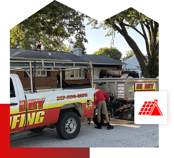 A roofing worker stands near a Be Dry Roofing truck in Quincy IL, while another person works on the roof of a house surrounded by trees; roofing equipment is visible, and a red roofing icon overlays the lower right corner, highlighting Roofing Services.